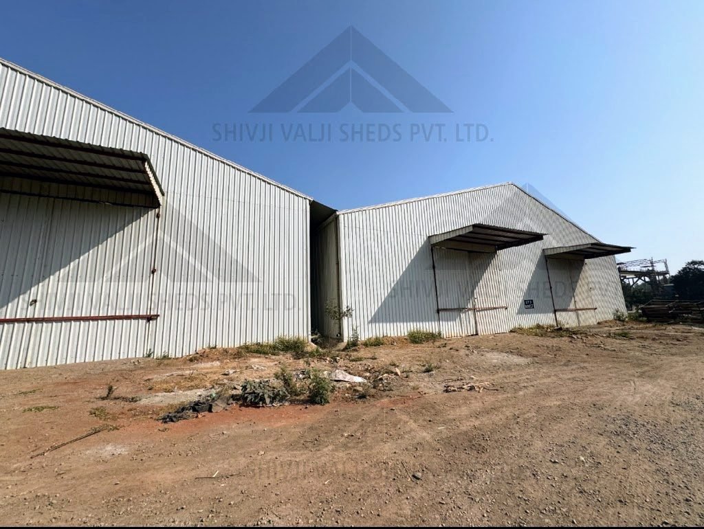 Side exterior of white corrugated-sheet clad sheds with door canopies against a clear blue sky