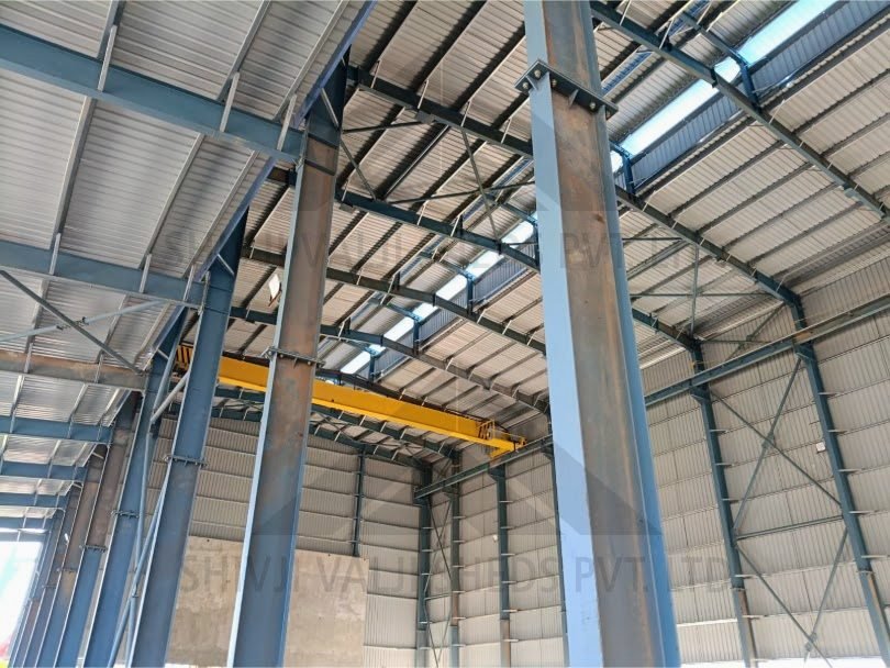 Interior of a tall I-section steel portal frame shed with yellow EOT crane, purlins, GI roof and wall sheeting with skylights