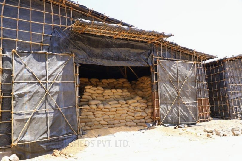Black HDPE tarpaulin shed on a bamboo frame with an open bay showing stacked sacks inside
