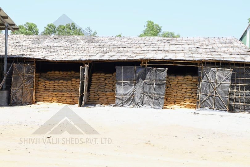 Long bamboo-framed shed with black tarpaulin walls and roof, bays full of stacked grain sacks