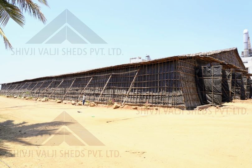 Side elevation of a long low black tarpaulin bamboo shed with a person for scale