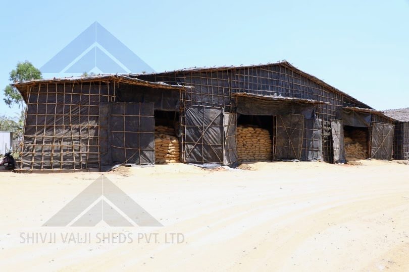 Exterior of a black tarpaulin bamboo shed with three open bays showing stacked sacks