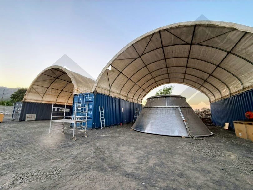 Wide dusk view of two arched white PVC dome shelters on blue shipping containers with a steel cone hopper and scaffold tower in front (810x608).