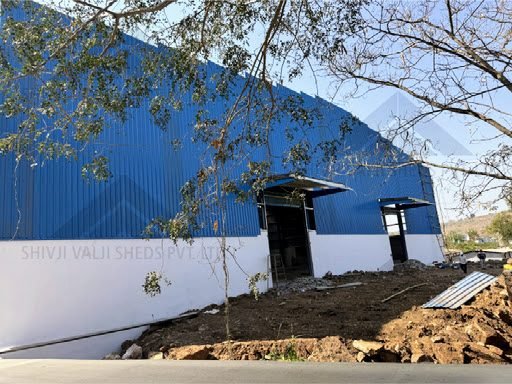 Single-storey gable-roofed shed clad in blue corrugated metal sheet over a white painted dado wall, with two open doorways